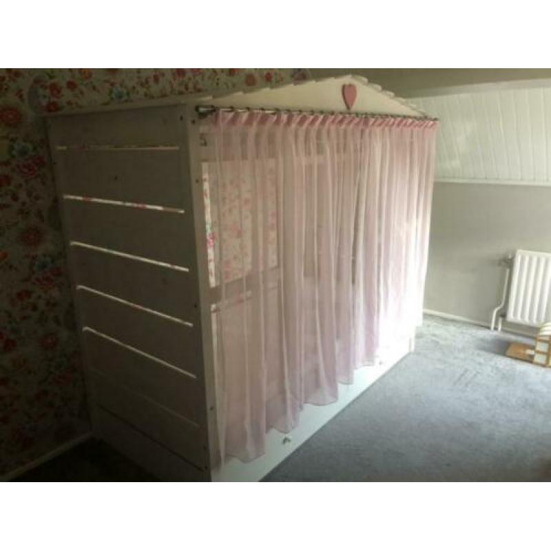 Gezellig wit bedhuis met roze gordijntjes en roze nachtlamp